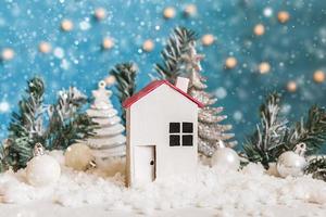 Abstract Advent Christmas Background. Toy model house and winter decorations ornaments on blue background with snow. Christmas with family at home concept. photo