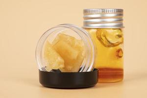 glass jar with brown cannabis wax, pieces of hardened resin of marijuana extract on an orange background photo