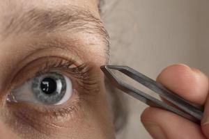 woman plucking eyebrow hairs with tweezers photo