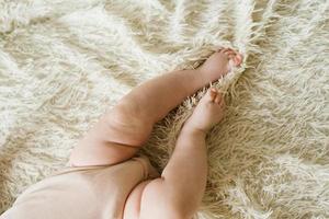 vientre y piernas de un bebé recién nacido en un traje de cuerpo acostado en una cama ligera, vista superior foto