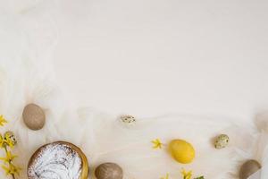 The Easter cake is decorated with powdered sugar, painted eggs on a beige and fabric background with a copy space. The eggs were colored beige with a decoction of nettle. Flat lay, top view photo