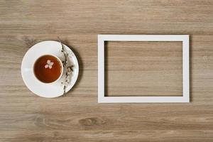 una taza blanca con té negro y una ramita de flor de manzana y un marco blanco sobre un fondo de madera. mocap y hasta prostranstva foto