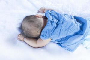 A child lies down on a white sheet in a blue shirt. photo