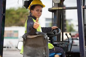 trabajadora conduciendo una carretilla elevadora en un almacén de contenedores industriales, levantó los pulgares hacia arriba, buen trabajo. foto