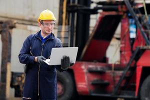 Young worker engineer wearing yellow safety hard hat using laptop computer laptop to checking and control loading containers box from cargo ship for import and export. photo