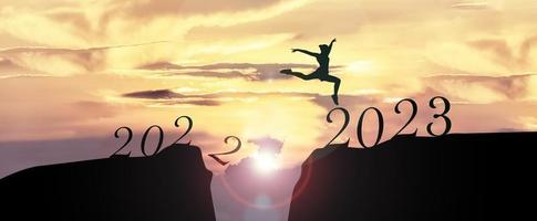 2023 Happy New Year concept, Young woman Jumping across the gap of the mountain from Old year 2022 to 2023 New Year. photo