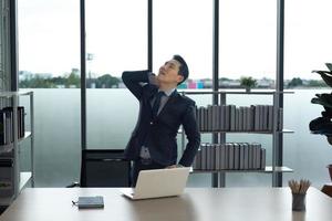 Asian Businessman in the office relaxing, stretching arm and neck muscle , waiting for working and meeting. photo