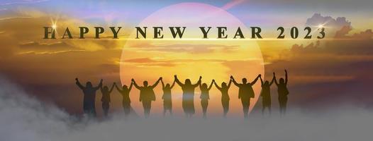Happy new year 2023, Keep fighting together, Silhouette of 2023 letters on the mountain with business people raised arms in teamwork concept at sunrise. photo