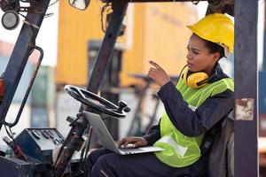 Female worker driving forklift and pointing hand in industrial container warehouse. photo