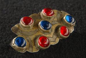 un broche antiguo con piedras preciosas, rojas y azules aisladas en un fondo negro, centroasiático foto