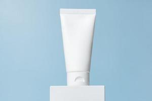 White cosmetic tube mockup. Plastic packaging for cosmetology cream product on a white podium on blue background. Skincare concept photo