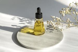 frasco de vidrio ámbar con pipeta cuentagotas con suero o aceite esencial en el podio de hormigón para la presentación del producto. cosméticos para el cuidado de la piel y plantas secas. concepto de belleza para el cuidado del cuerpo facial. foto