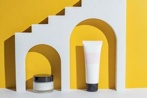 productos cosméticos de belleza en arco blanco sobre fondo amarillo. embalaje sin marca adv. tarro de crema y tubo. foto