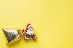 A toy Santa with a gold sack of gifts on yellow background with copy space. The concept of Christmas new year. photo