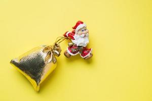 A toy Santa with a gold sack of gifts on yellow background with copy space. The concept of Christmas new year. photo
