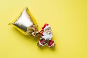 A toy Santa with a gold sack of gifts on yellow background with copy space. The concept of Christmas new year. photo