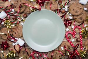 Chocolate chip cookies Christmas canes caramel red gold scenery and marshmallow on wooden background empty plate. Copy space Frame.