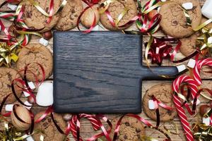 Chocolate chip cookies Christmas canes caramel red gold scenery and marshmallow on wooden background. Copy space Frame. photo
