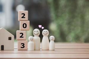 2023 feliz año nuevo. familia feliz, planificación presupuestaria, seguros, casa y bienes raíces, plan y ahorro de dinero para el futuro. familia de figuras humanas con cara sonriente y corazón con bloques de madera número 2023. foto