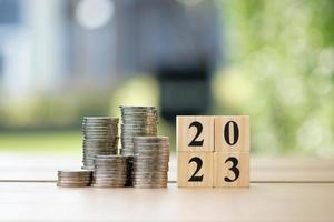 2023 Happy New Year. Business and saving money, Financial growth, interest rate increase, inflation, sale price and tax rise concept. Coins stack and wooden blocks number 2023 on blur background. photo