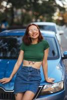 hermosa chica se sienta en el capó de un coche azul foto