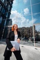 Young woman walking with a laptop by the modern building photo