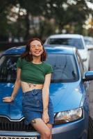 Beautiful girl sits on the hood of a blue car photo