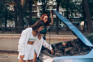 dos mujeres con auto roto en la carretera. capucha abierta foto