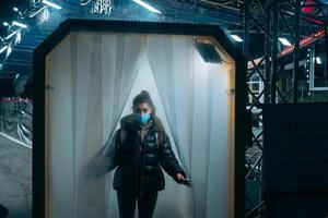 mujer con máscara médica se queda en un túnel de desinfección foto