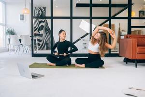 Two young women meditating in lotus pose at home photo