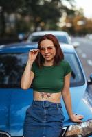 Beautiful girl sits on the hood of a blue car photo