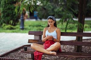 mujer usando un teléfono inteligente en el parque sentado en un banco foto