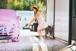 Brunette from a high-pressure hose applies a cleaner on the car photo