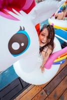 Happy young woman sitting on inflatable unicorn toy mattress photo