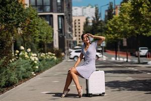 Pretty young woman sits on suitcase outside. photo