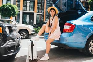 Woman packing her suitcase into luggage boot of the car. photo