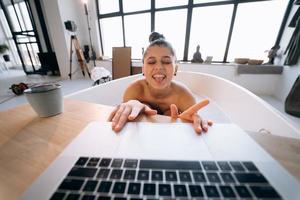 Young woman working on laptop while taking a bathtub photo