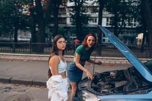 Two women with broken car on the road. Open hood photo