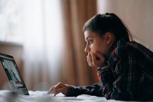 mujer joven trabaja mientras tiene una laptop acostada en la cama foto