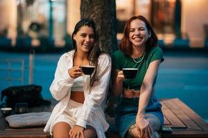 Best friends sitting on the park bench drinking coffee. photo