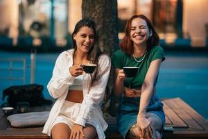 Best friends sitting on the park bench drinking coffee. photo