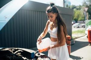 Young woman pouring antifreeze car screen wash liquid into car photo