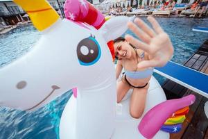 Happy young woman sitting on inflatable unicorn toy mattress photo