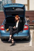 Woman working on laptop while sitting in trunk of car photo