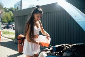 Young woman pouring antifreeze car screen wash liquid into car photo