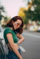 bella joven de moda con gafas posando cerca del coche foto