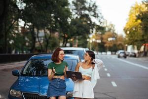 Two young women with a laptop near the car photo