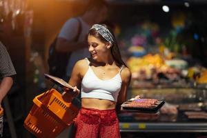 mujer joven elige carne en una tienda de comestibles foto