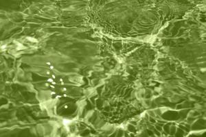 Defocus blurred transparent green colored clear calm water surface texture with splashes and bubbles. Trendy abstract nature background. Water waves in sunlight with copy space. Green watercolor shine photo
