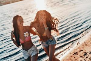 Playful girls. Two attractive young women in swimwear smiling while walking on the beach photo